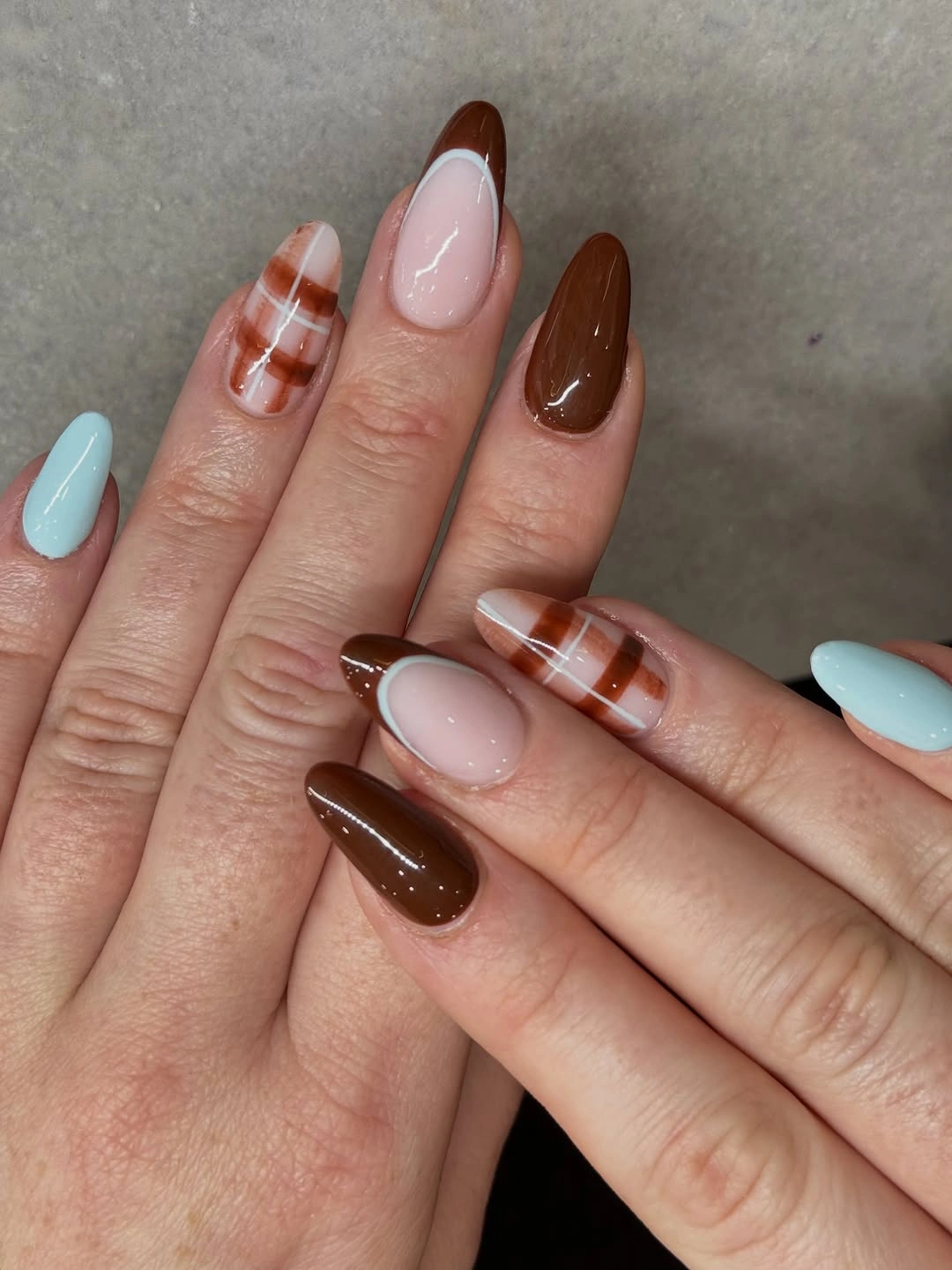 Medium almond nails with pale blue, nude, brown, and orange plaid accents