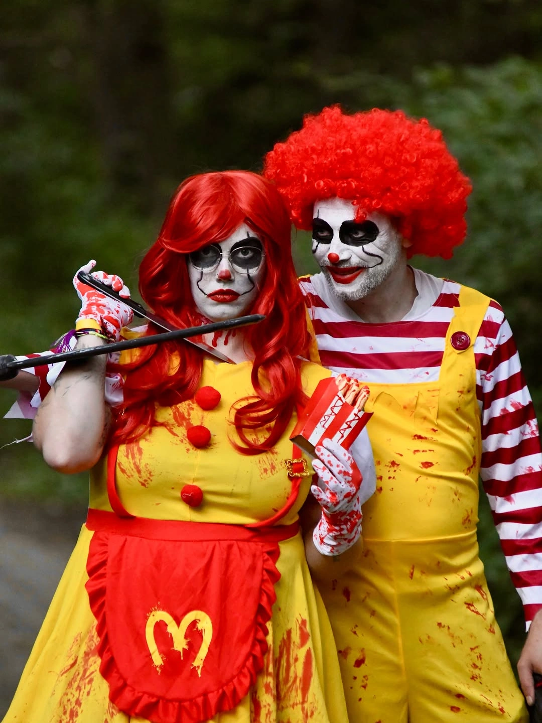 Couple in bloody Ronald McDonald horror Halloween costumes with red wigs