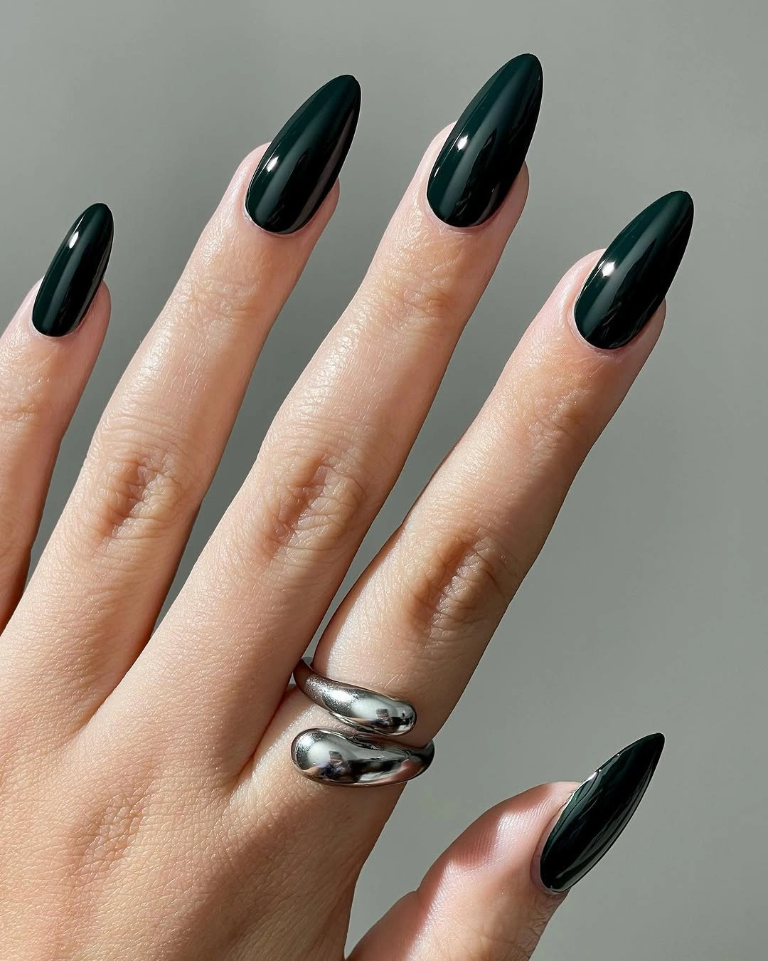 Long glossy forest-green almond nails with silver rings