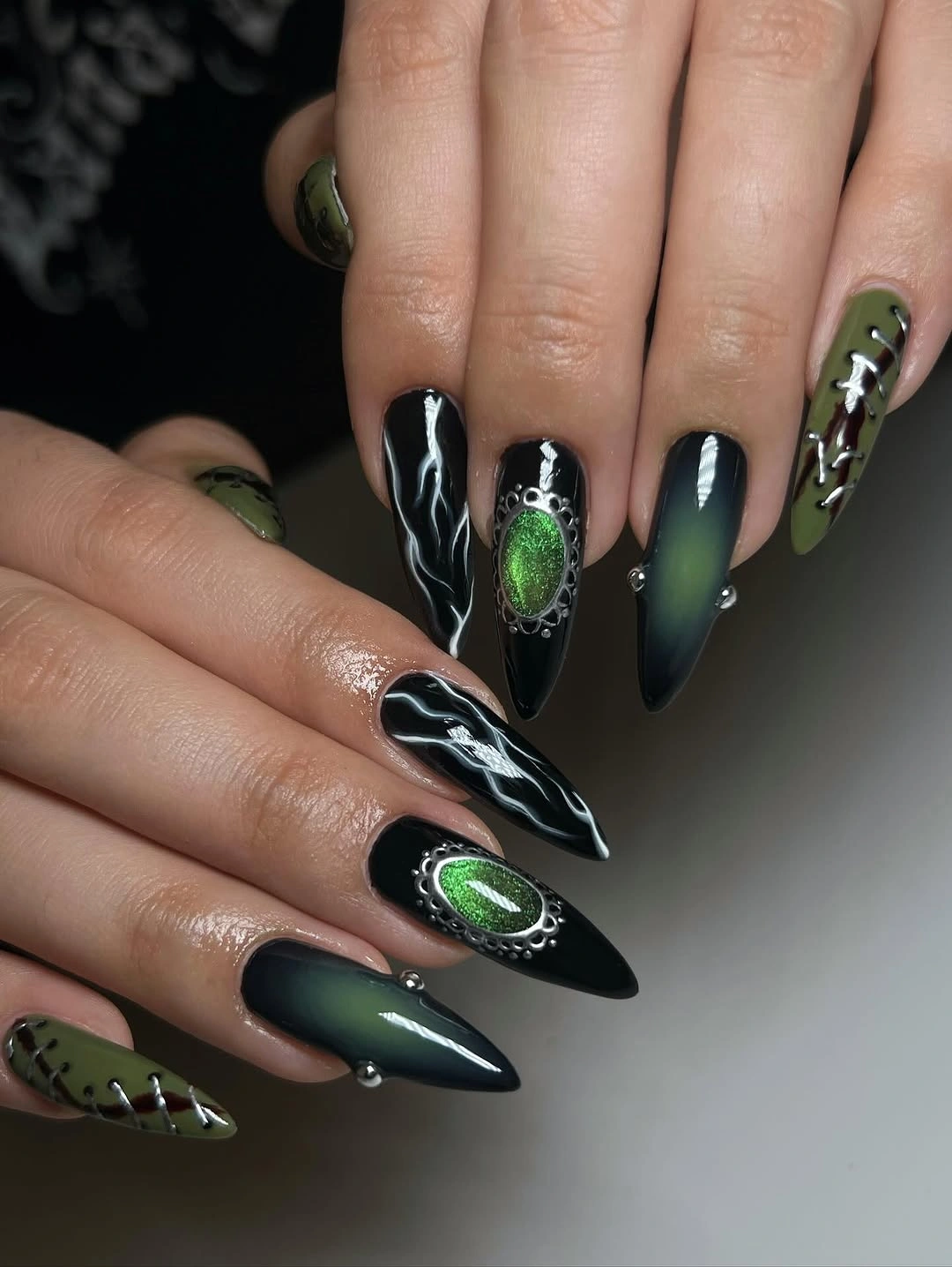 Black and green pointed nails with emerald oval accents