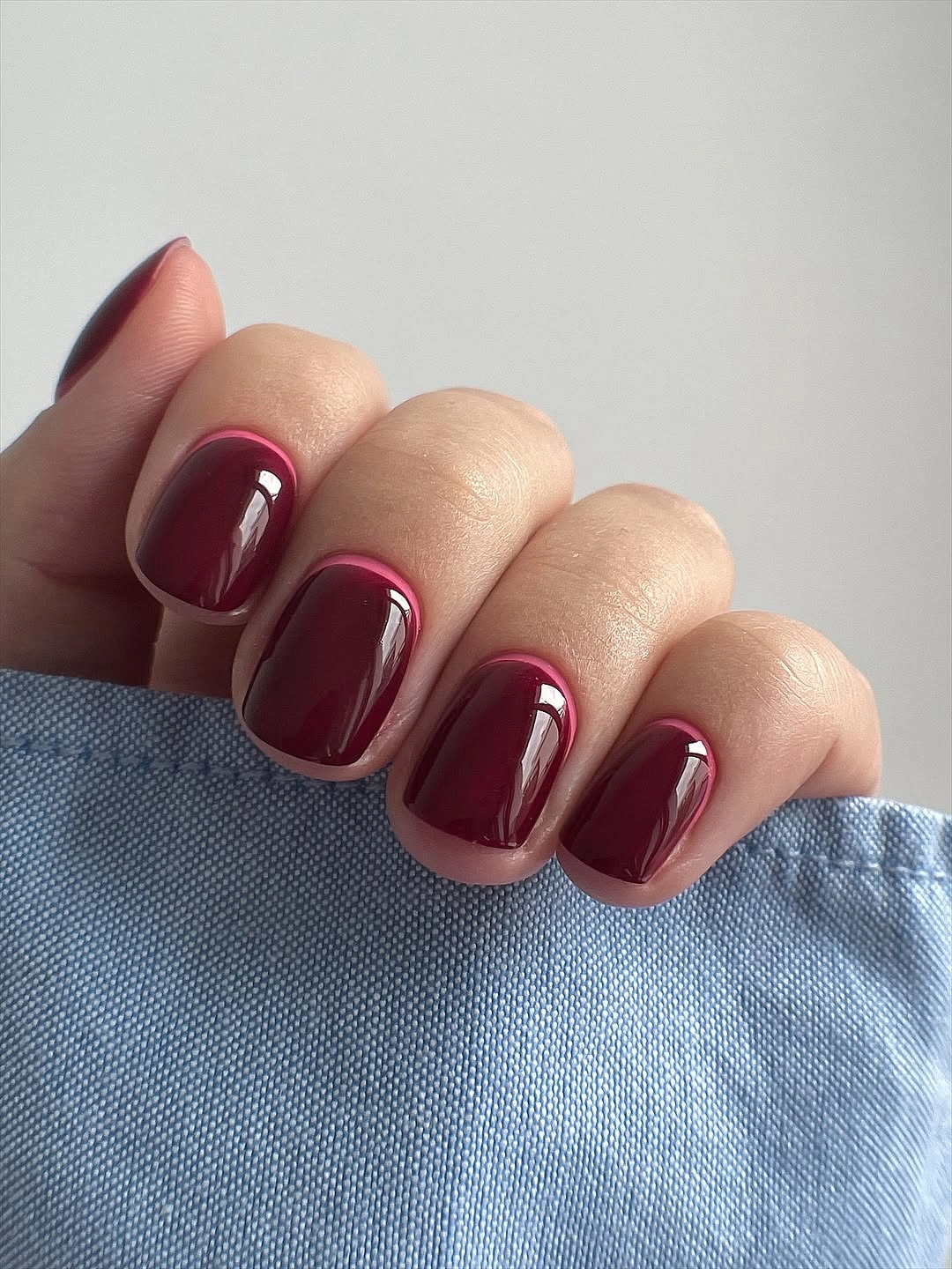 Short glossy burgundy rounded-square nails with denim contrast