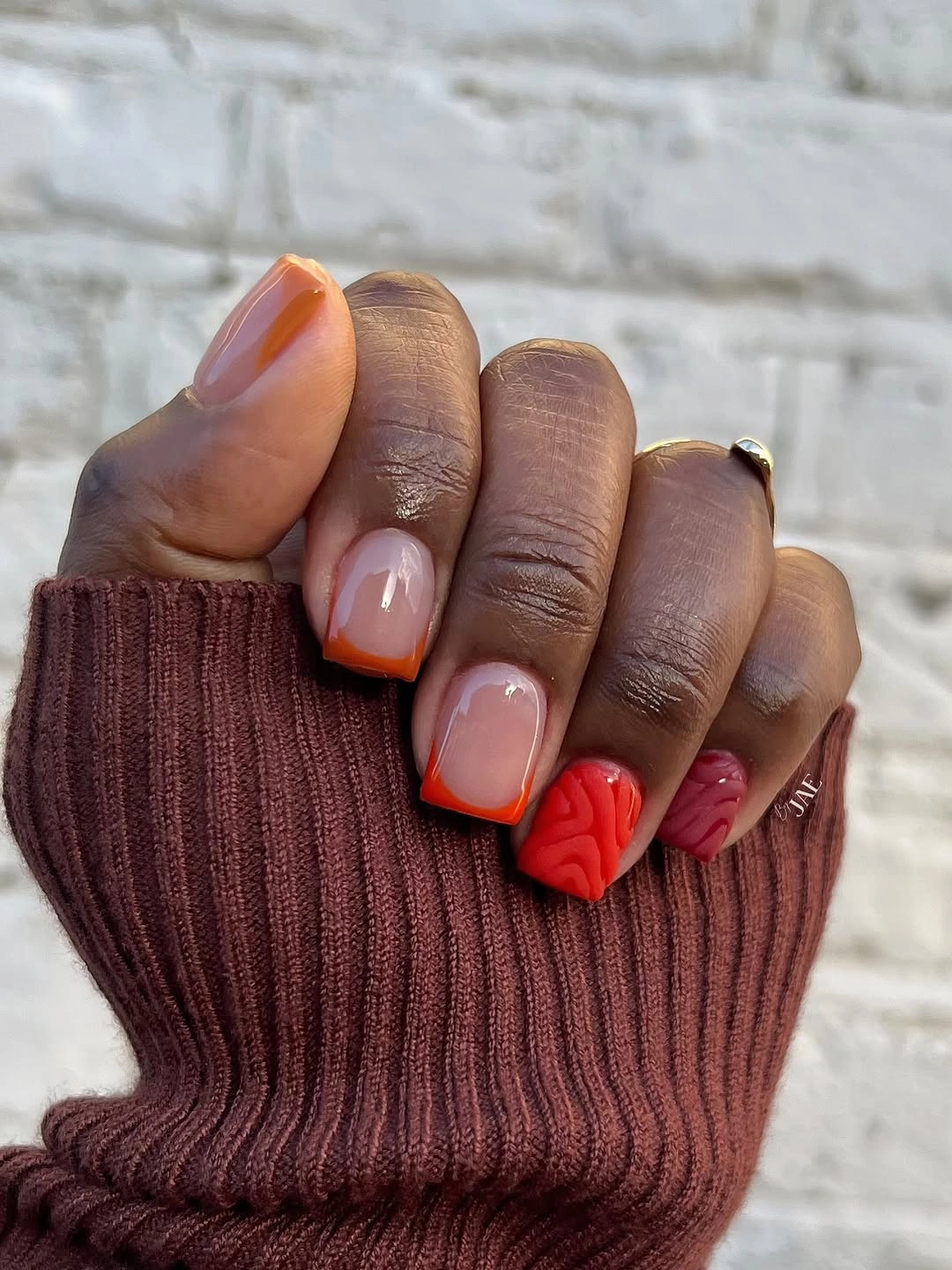 Short rounded nails with orange edges and one red flower accent
