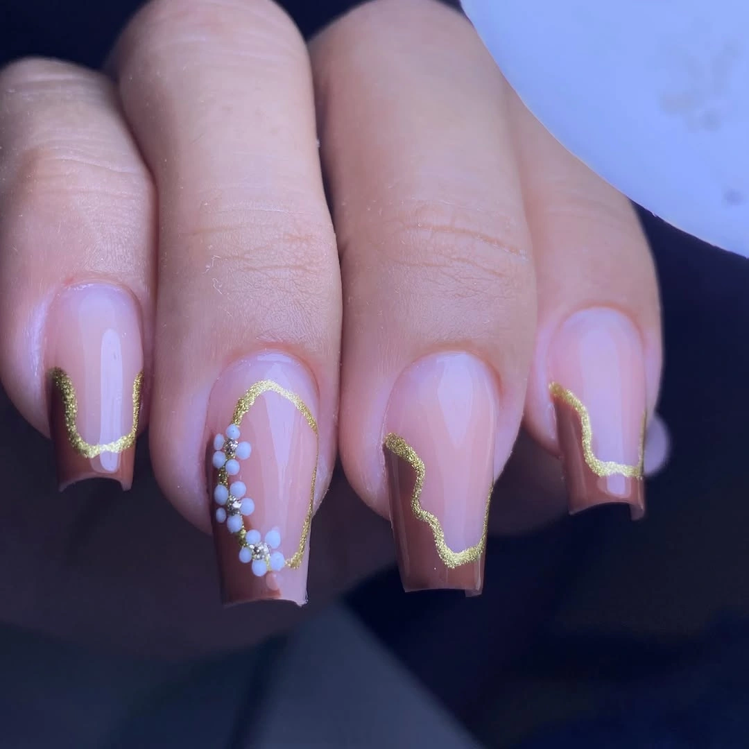 Short blush square nails with gold waves and a jeweled accent