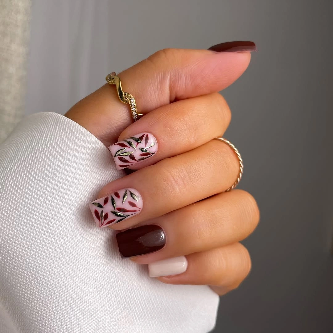 Rounded-square burgundy nails with ivory leaf accents