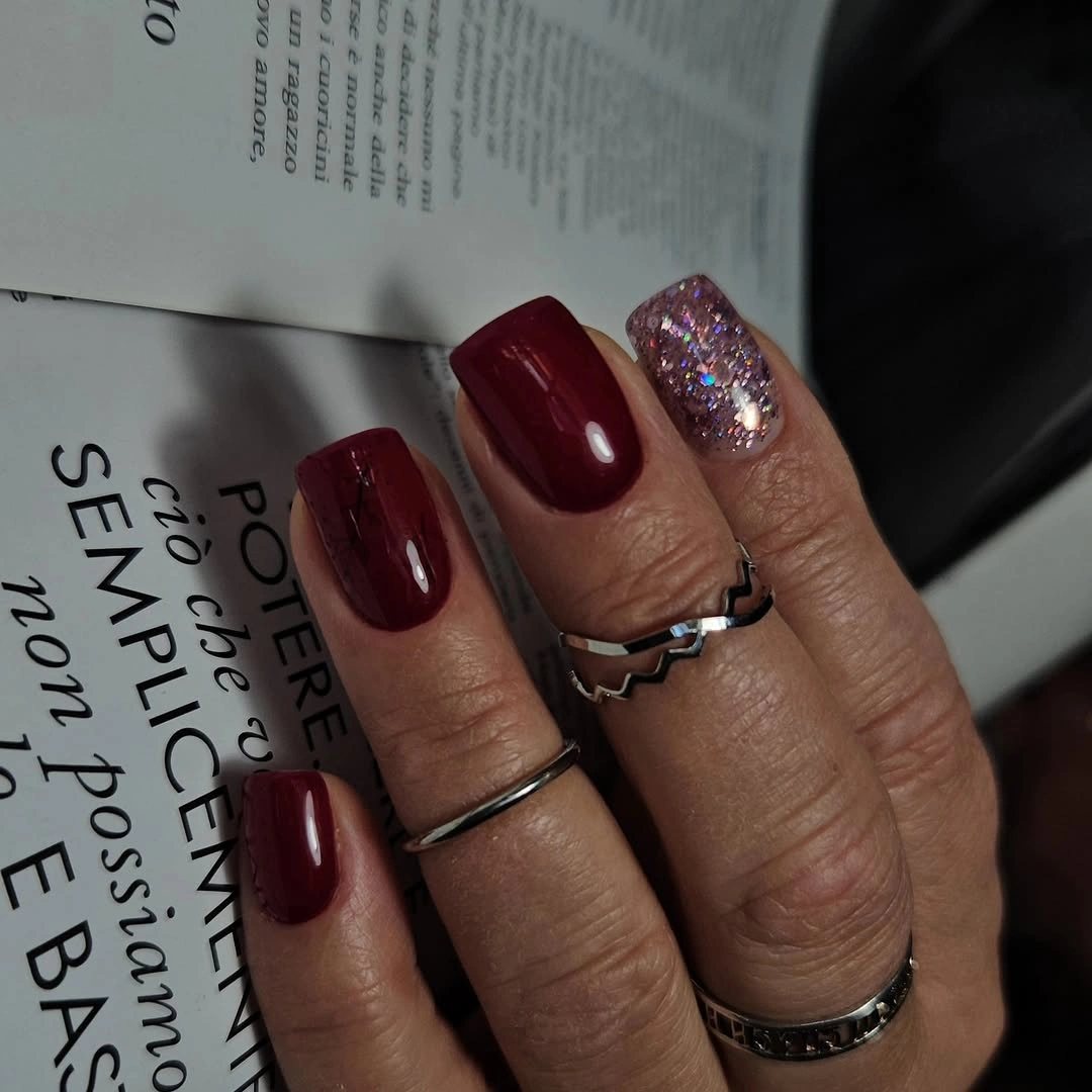Short square burgundy nails with one multicolor glitter accent