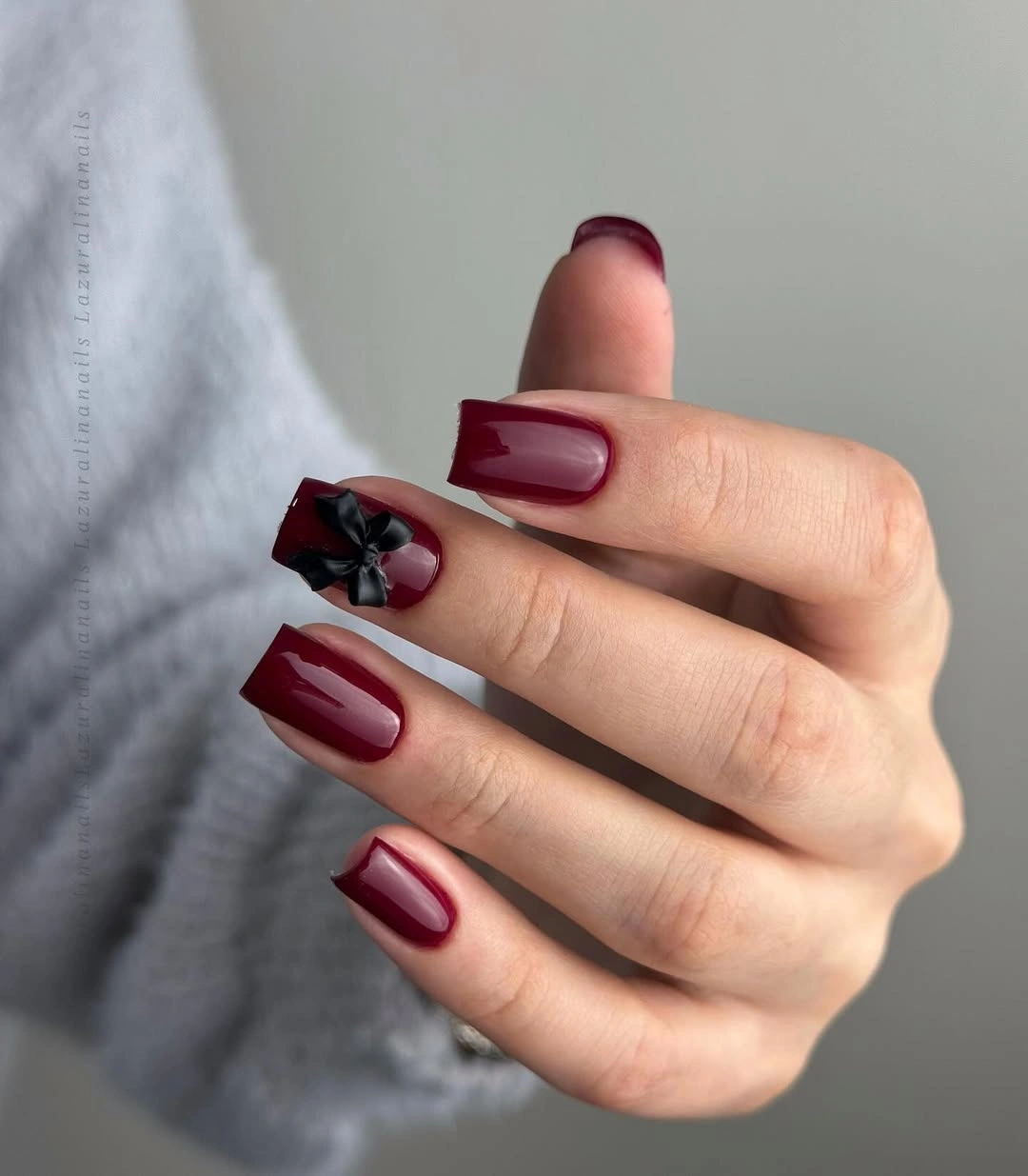 Short square burgundy nails with one raised black bow