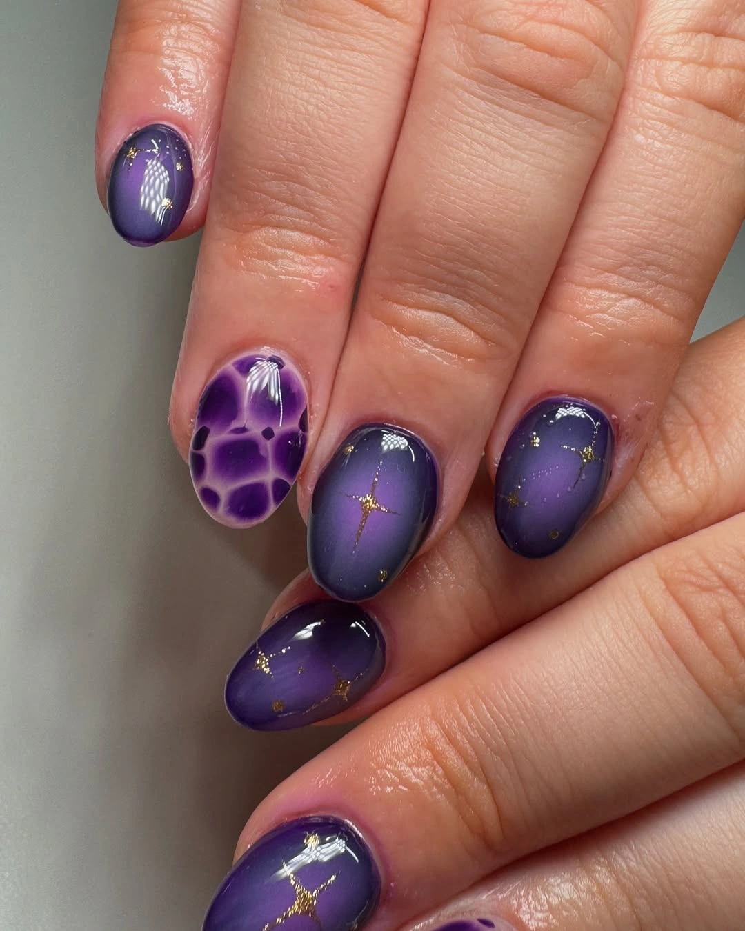 Short rounded violet nails with one pale floral accent