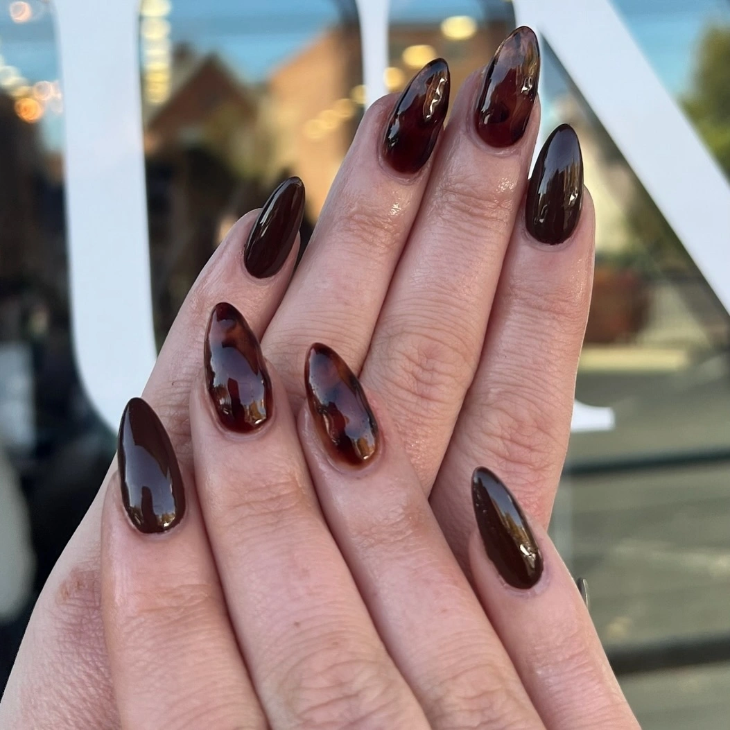 Long almond nails in glossy deep brown with mottled amber tortoiseshell-like details