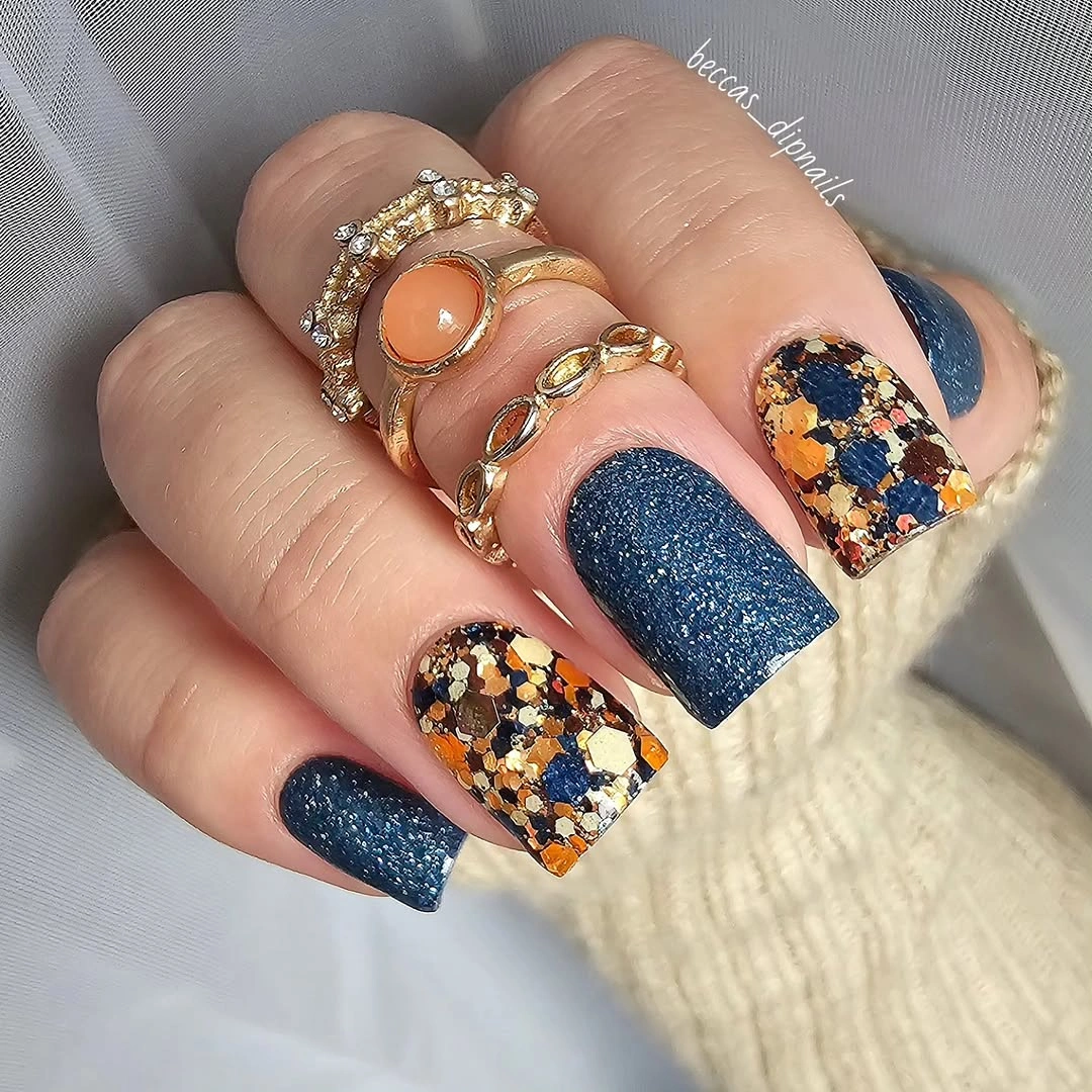 Medium square nails with navy sparkle-like polish and warm patterned accent nails