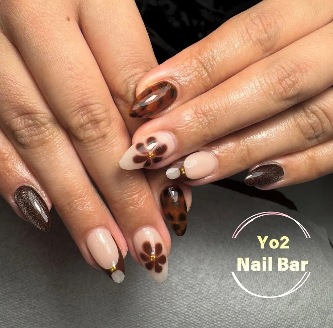 Nude almond nails with cocoa brown floral-style details and cream accents