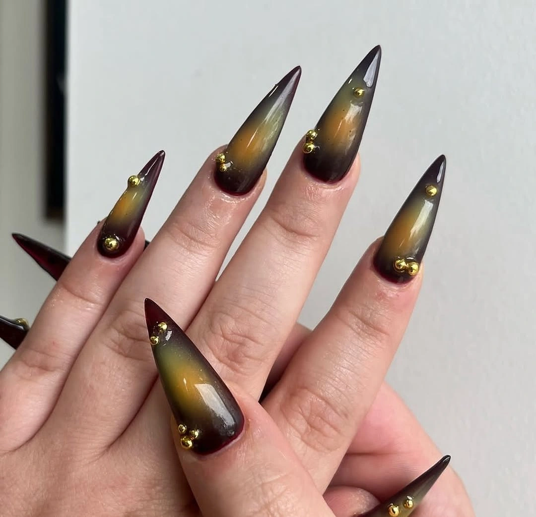Long pointed nails with deep burgundy edges golden yellow centers and small round accents