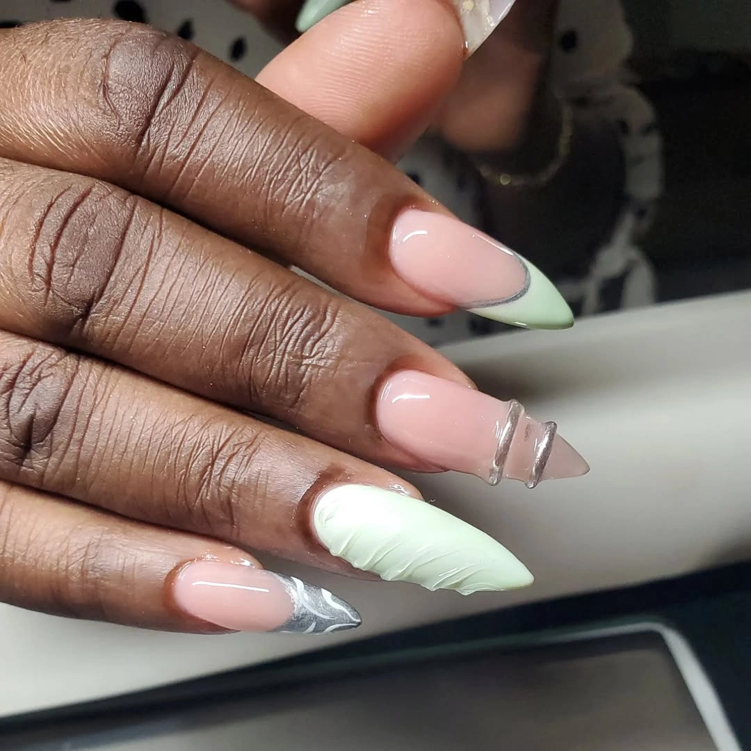 Long nude pointed nails with green tips and white textured accent