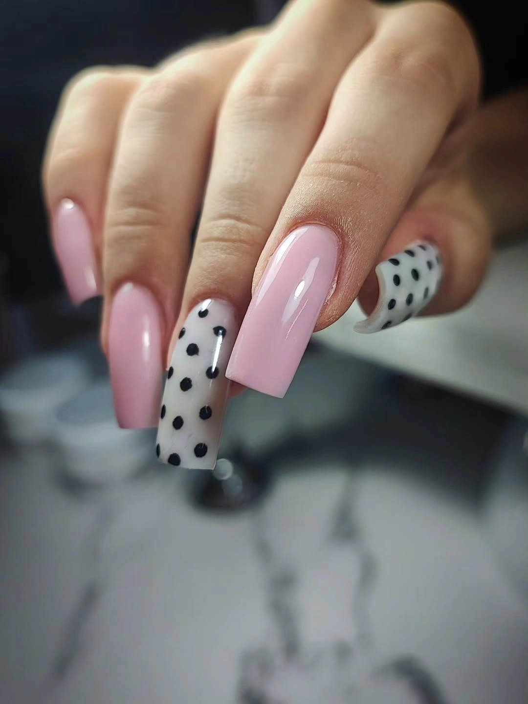 Long pale pink nails with a black and white polka dot accent