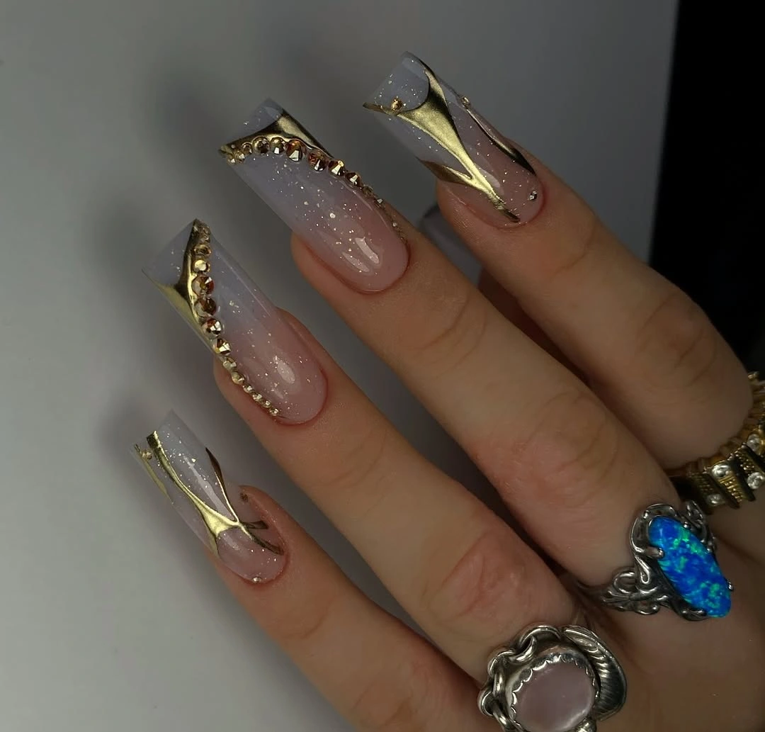 Long nude nails with fine gold framing and a dark blue accent