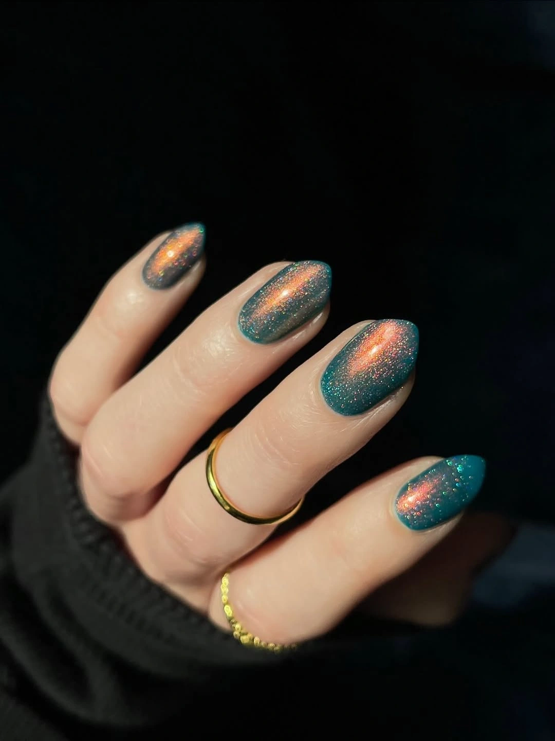 Reflective deep teal almond nails against a dark background