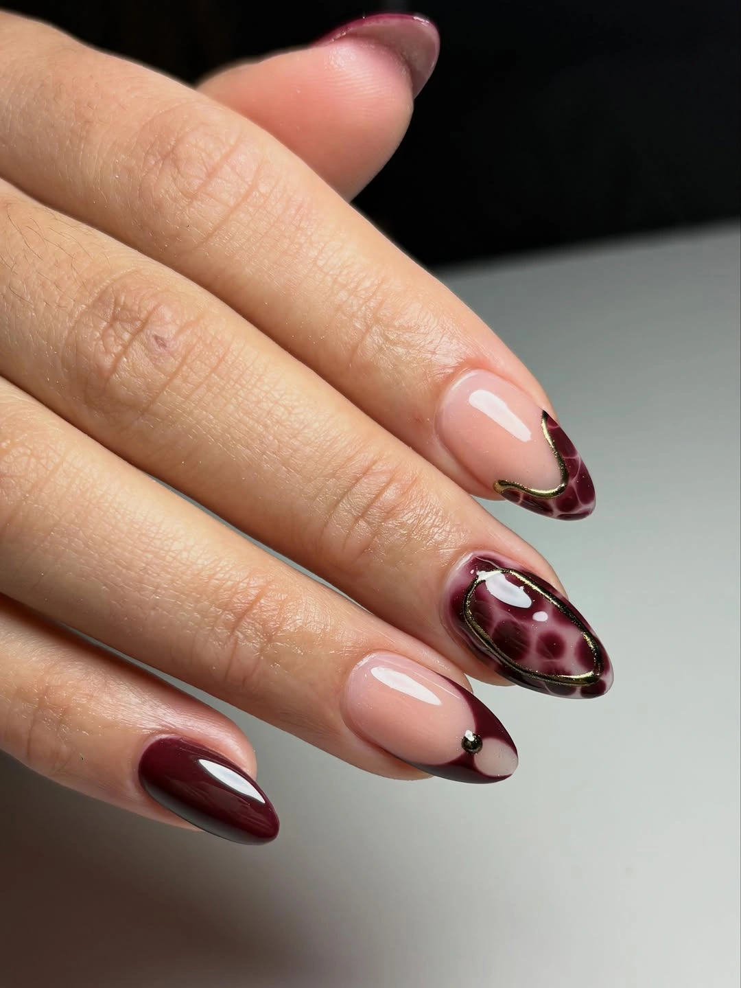 Blush almond nails with oxblood curved tips and spotted accent