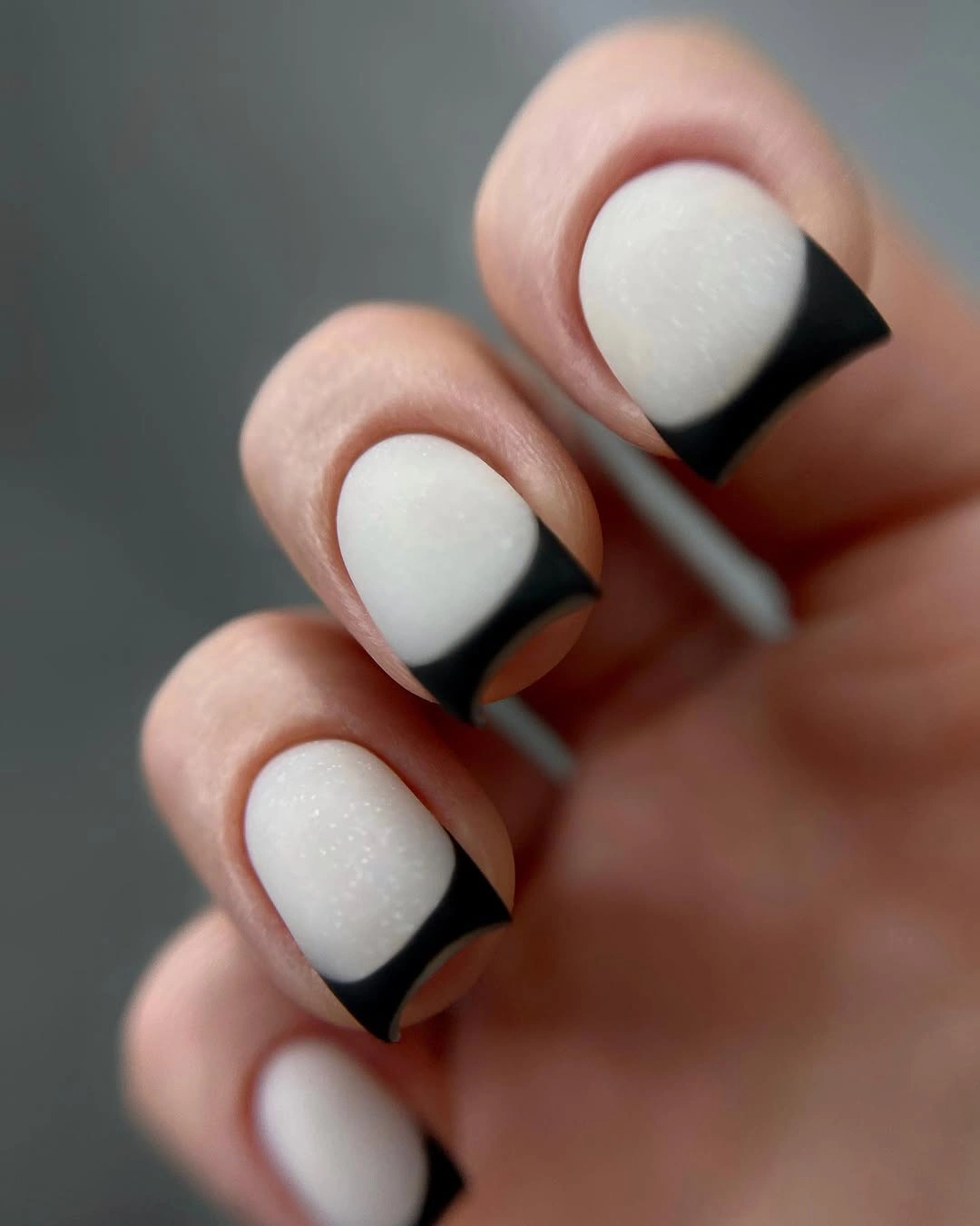 Short pale matte nails with bold black curved French tips