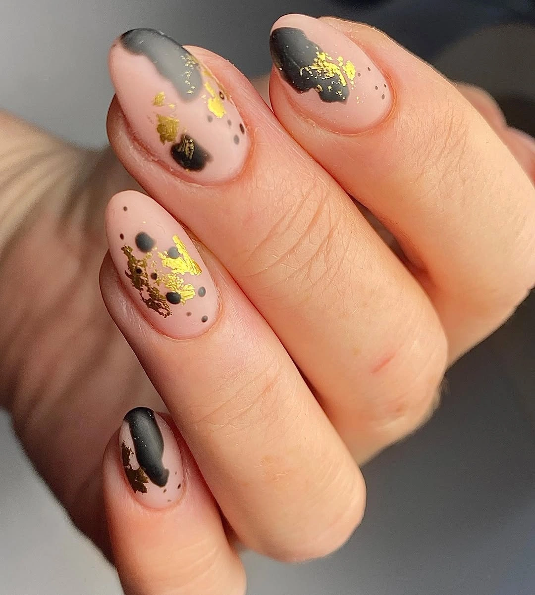 Short nude almond nails with charcoal patches and gold flecks