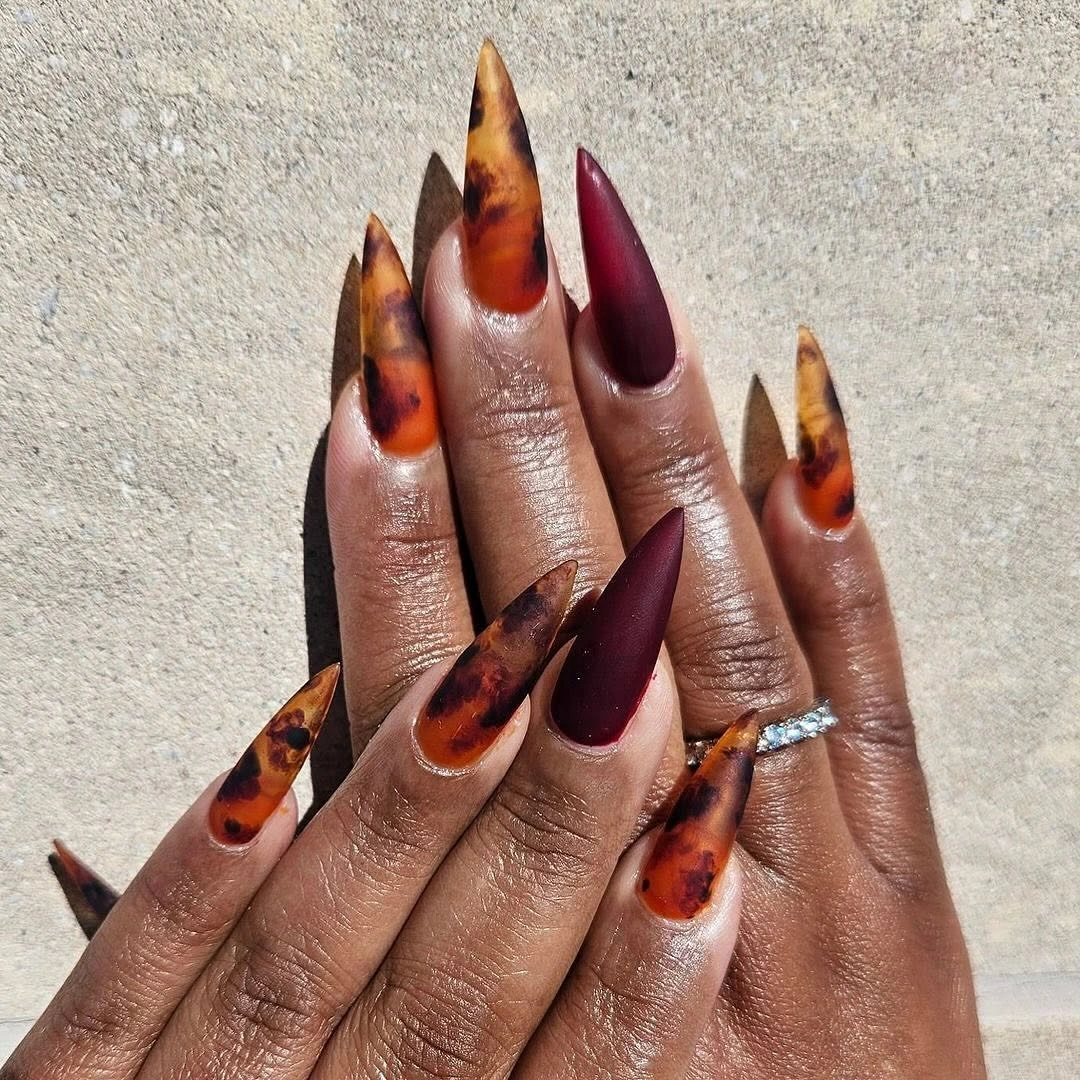 Long stiletto nails alternating burgundy and warm tortoiseshell accents