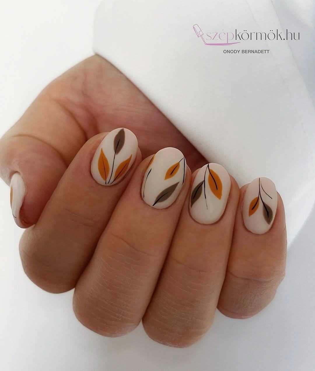 Short creamy white nails with small brown and orange leaf accents