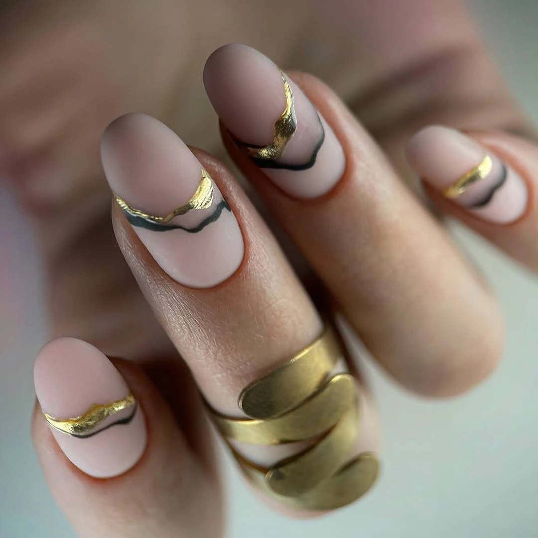 Pale pink matte nails with irregular black and gold curved accents