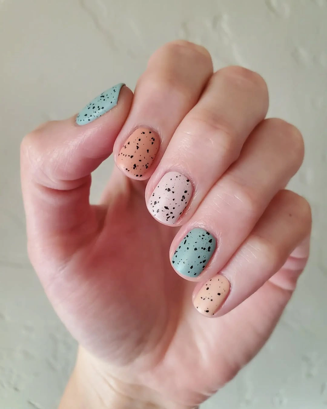 Short pastel aqua peach and pink nails with fine dark speckles