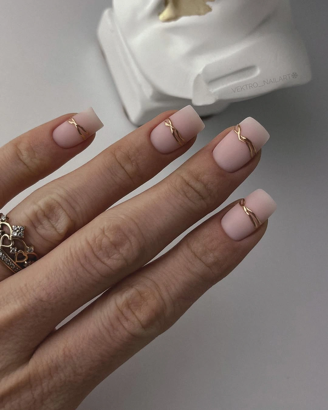 Short beige matte nails with delicate gold curves near the tips