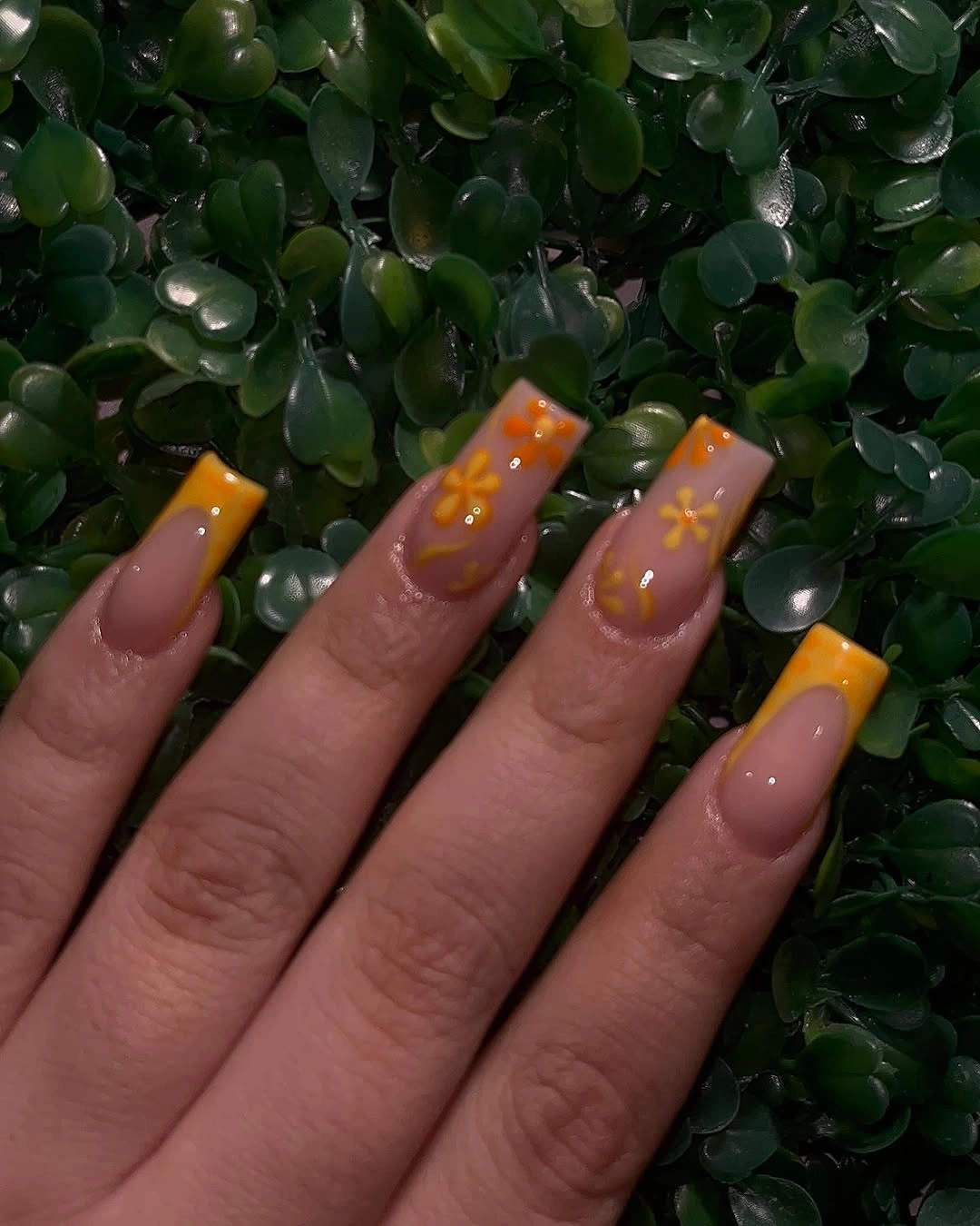 Medium square nude nails with orange tips and tiny floral accents