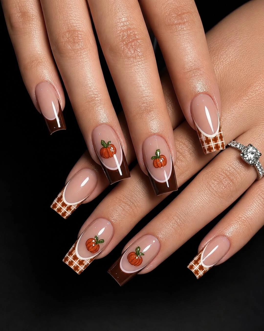 Almond nails with brown checkered tips and tiny orange pumpkin accents