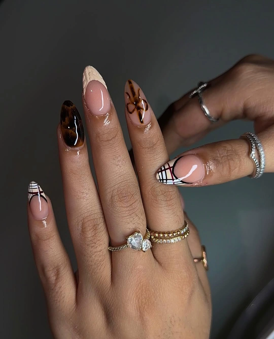 Medium almond nails with dark tips and two neutral patterned accents