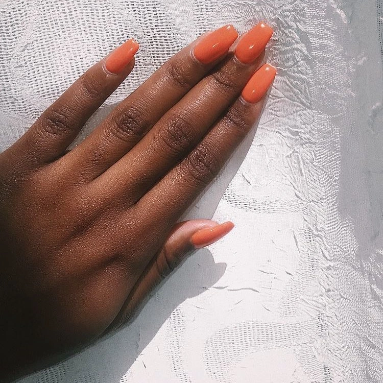 Long almond nails in a warm glossy orange-coral shade