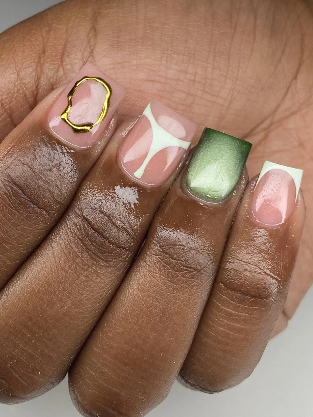 Short rounded-square pink nails with green, gold, and white details