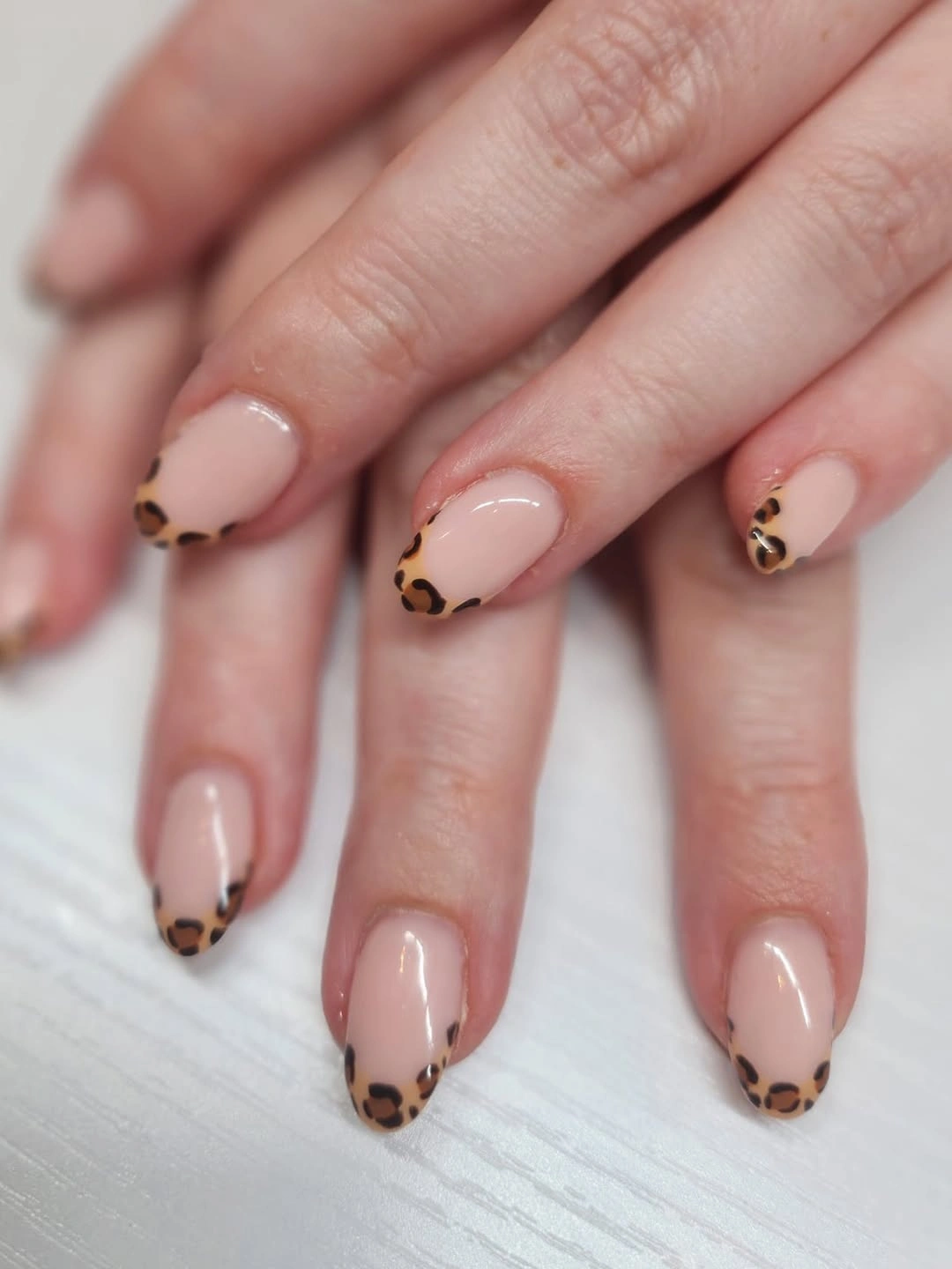 Medium nude nails with small brown and black leopard-style tip accents
