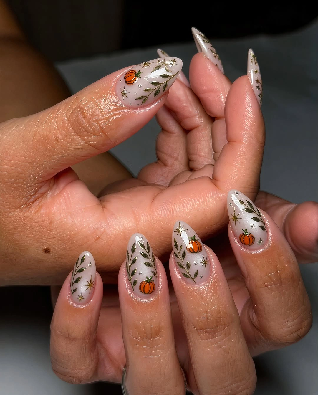 Long white stiletto nails with small orange pumpkin and green botanical details