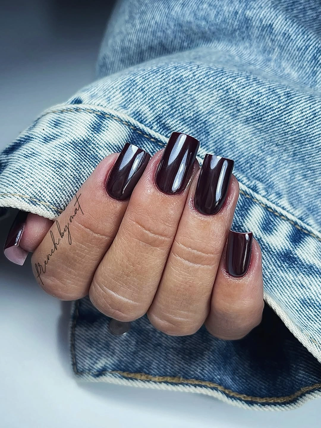 Medium square nails in a uniform deep glossy plum shade against denim