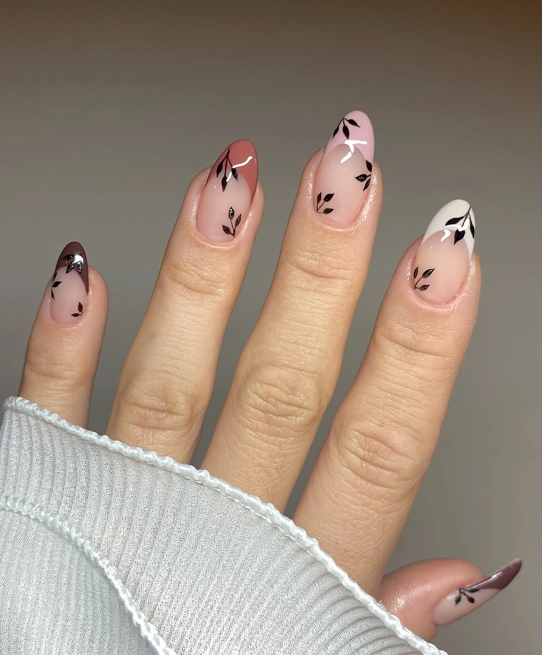 Pale nude almond nails with small dark botanical marks near tips