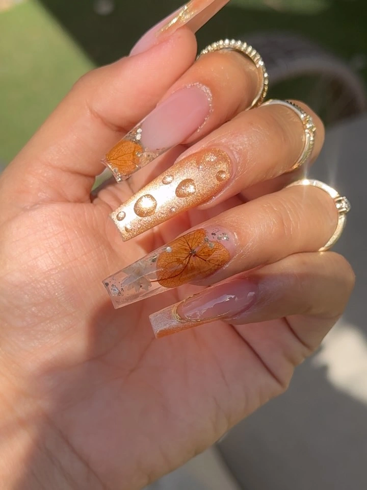 Clear pink square nails with orange leaves gold dots and sparkle