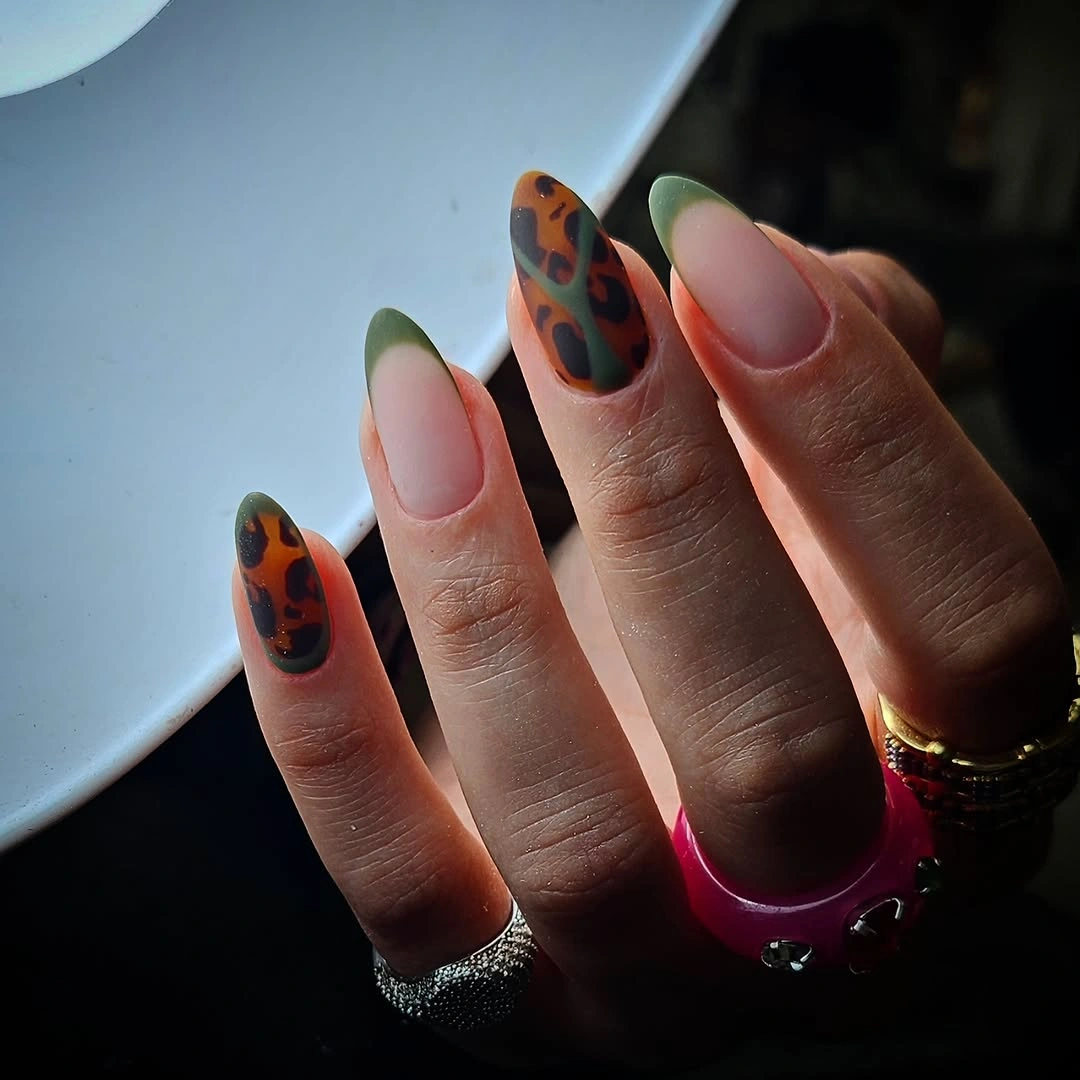 Long almond nails with green borders nude centers and warm patterned accents