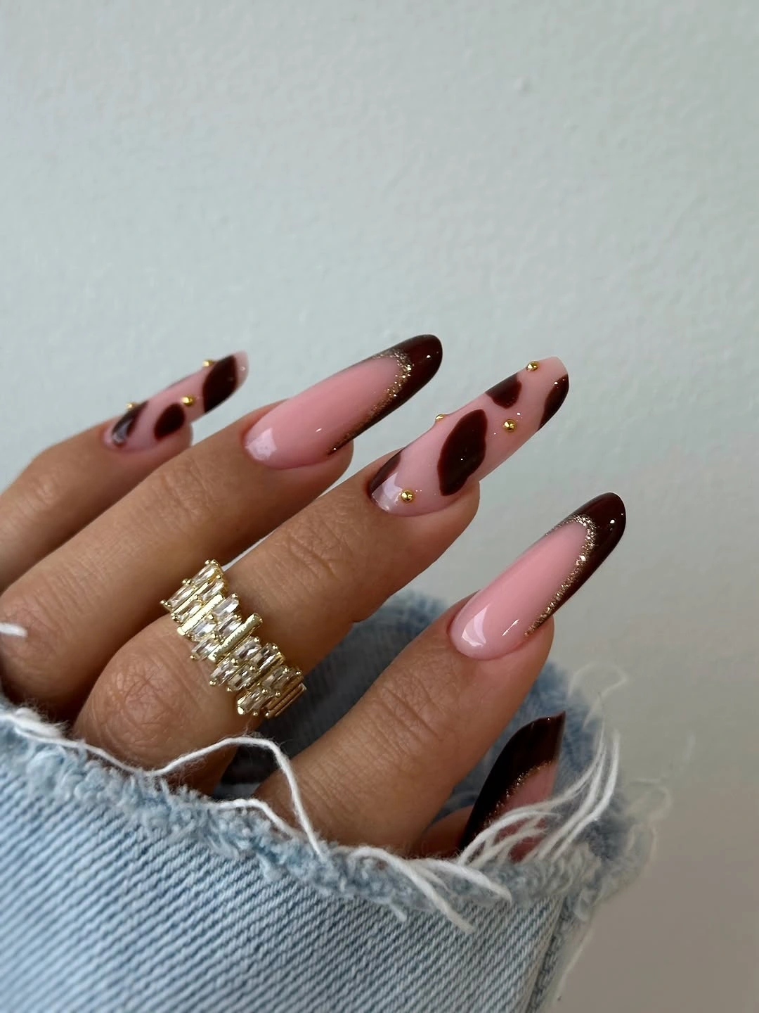 Long pink almond nails with deep brown curved French edges and gold dots