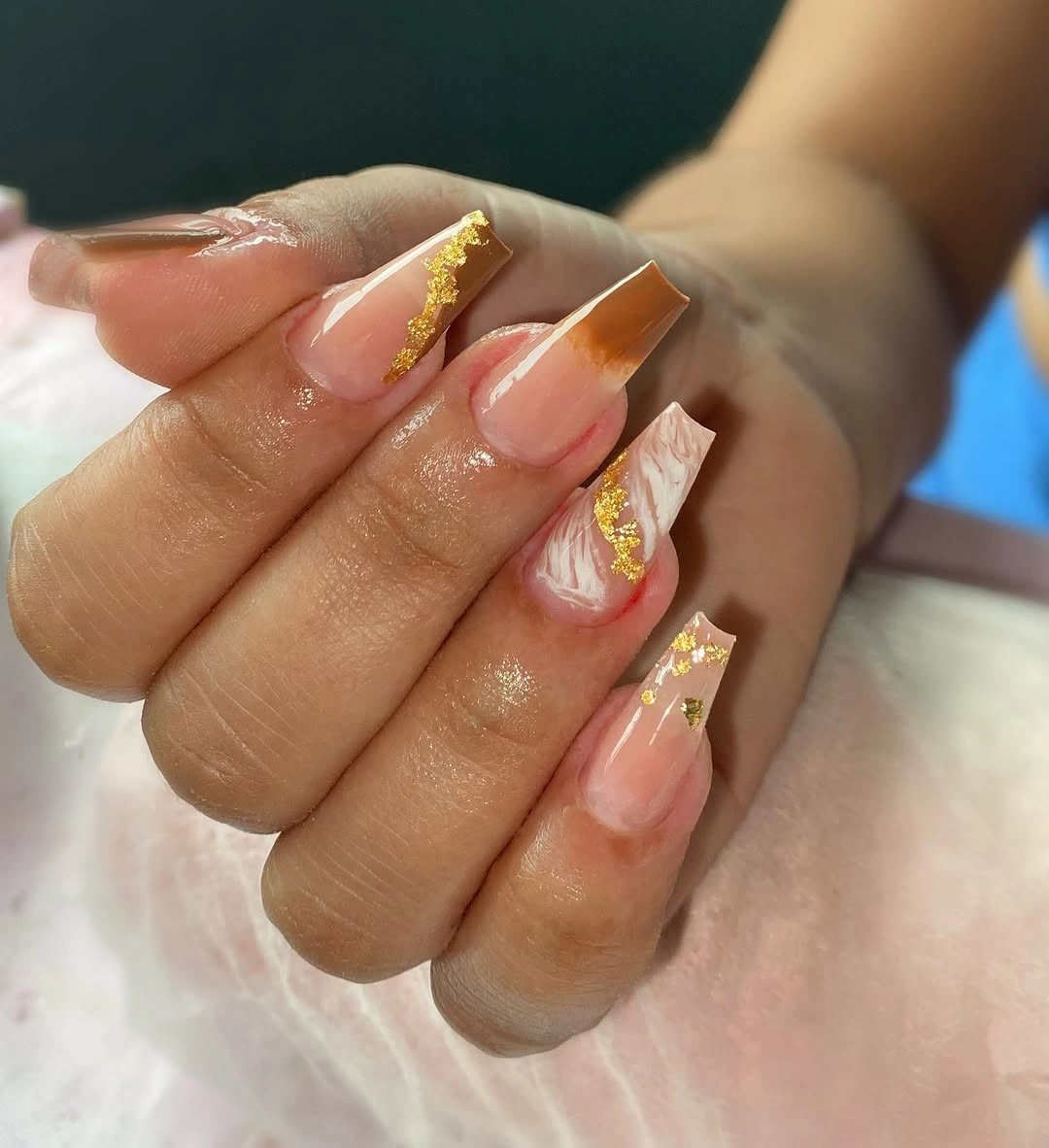Long translucent pink nails with gold glitter trails and warm lines