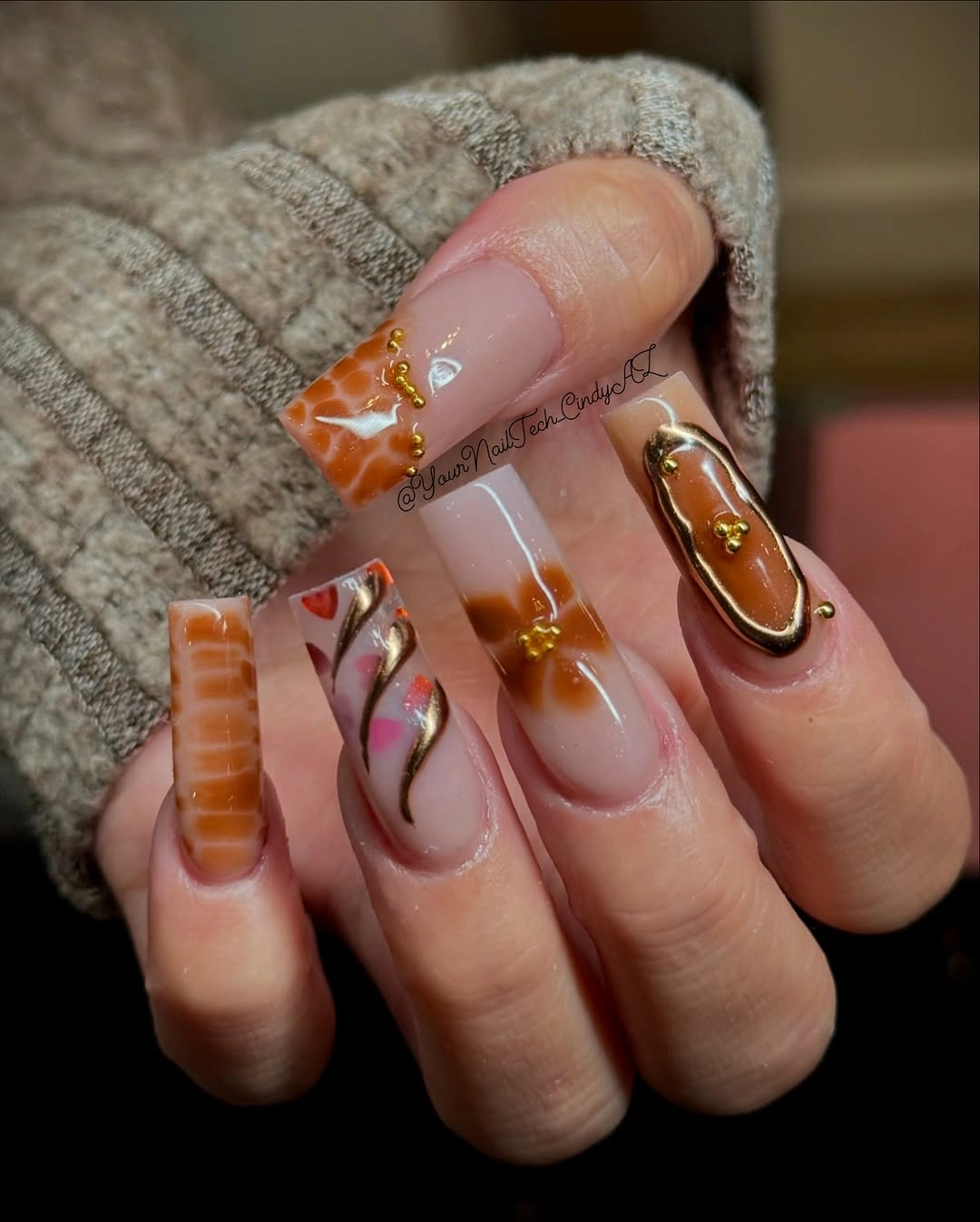 Translucent pink almond nails with warm amber swirls and gold accents