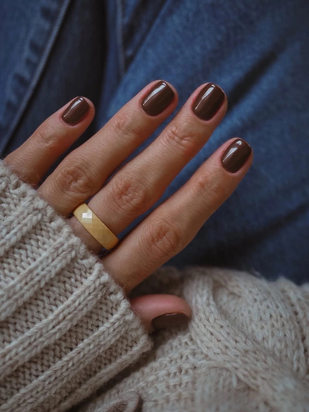 Short rounded glossy chocolate brown nails against blue denim