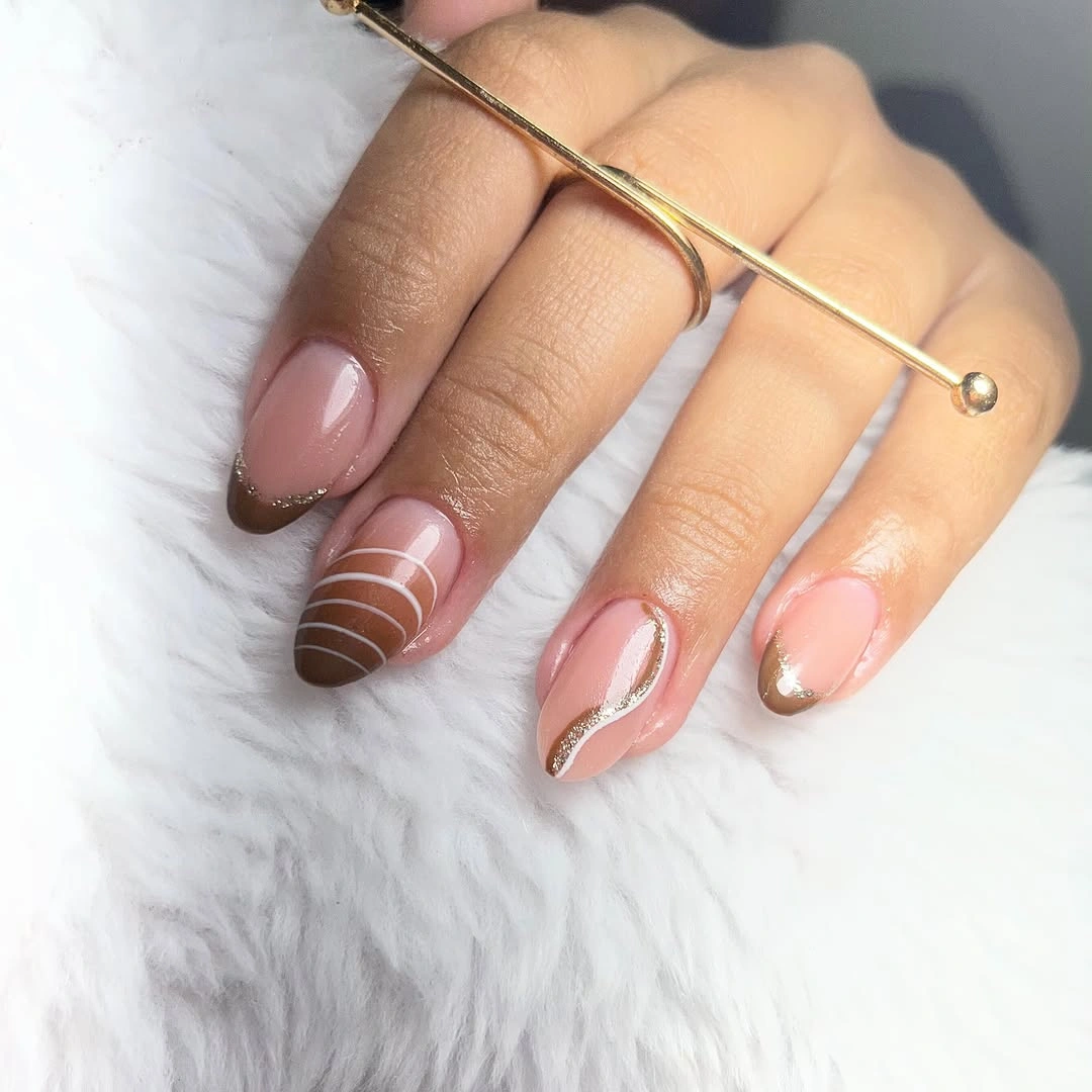 Warm nude nails with thin white curved lines and subtle gold details