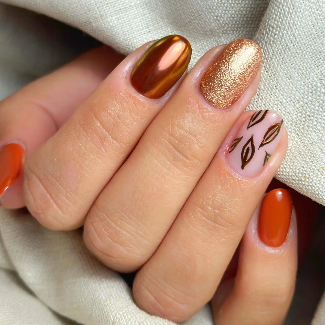 Short burnt orange brown and leaf-print nails with one gold glitter accent