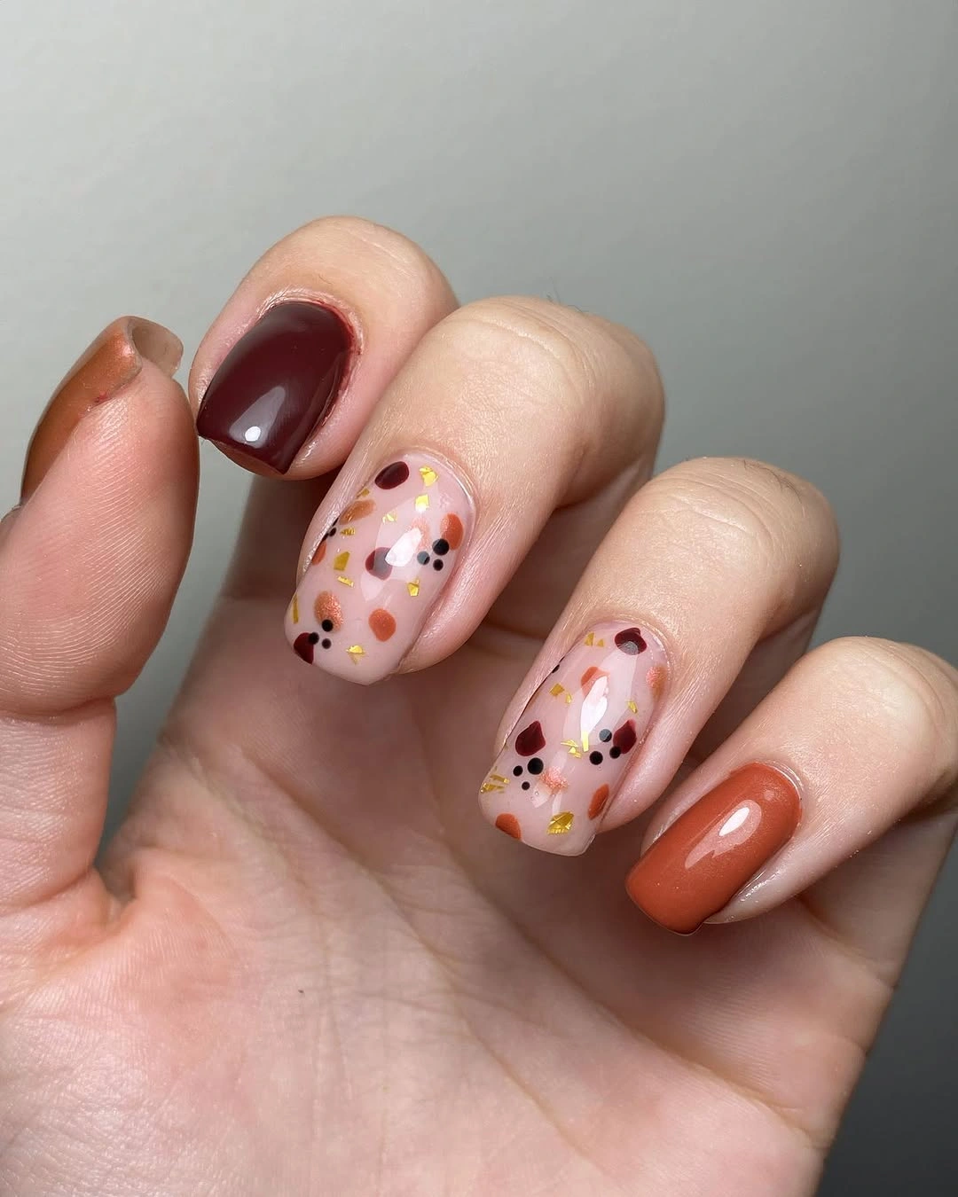 Burgundy terracotta and nude almond nails with warm confetti dots