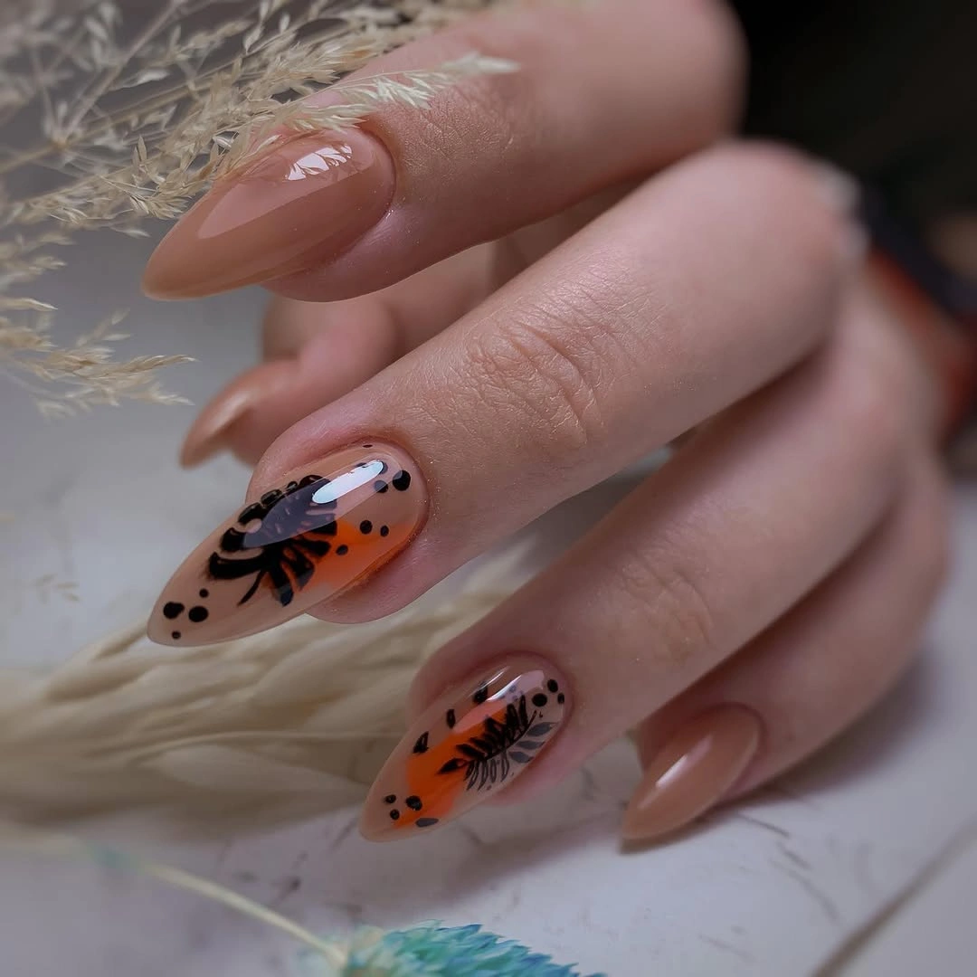 Long nude almond nails with sharply outlined black leaf motifs and warm accent