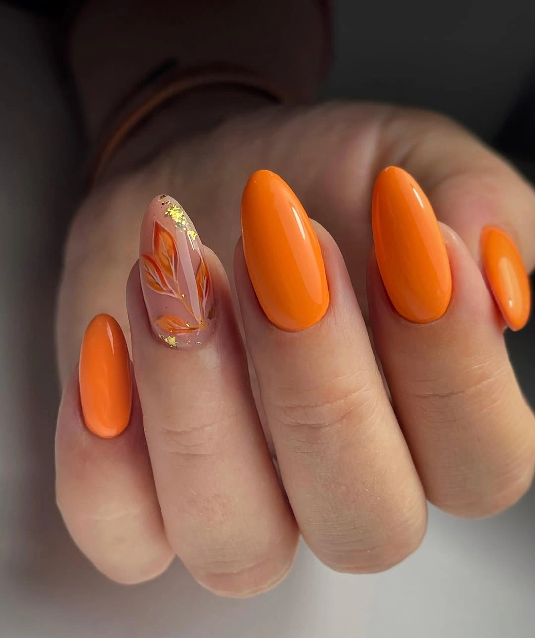 Medium almond bright orange nails with one warm botanical nude accent