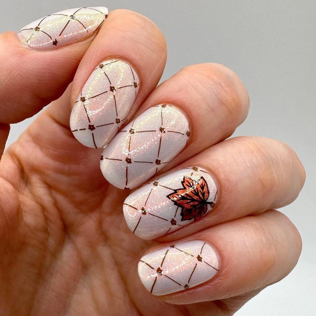Pale rounded nails with fine brown grid and leaf accent