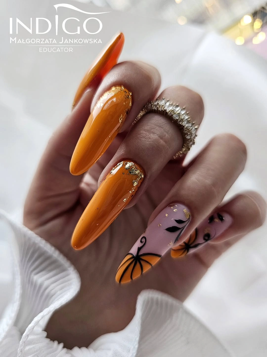 Orange stiletto nails with pumpkin line art and crystal accents