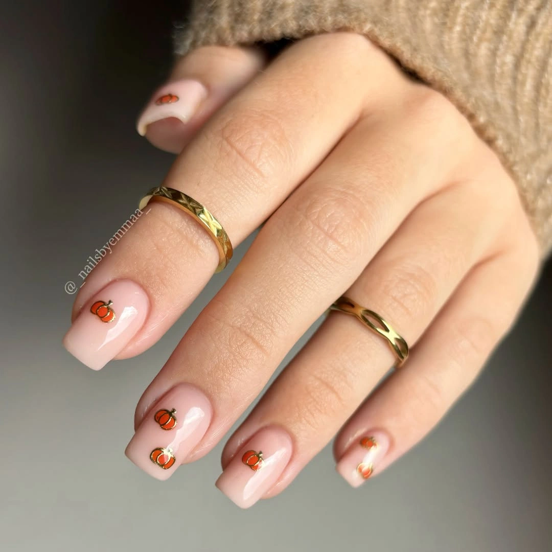 Short pale pink nails with tiny gold-outlined pumpkins